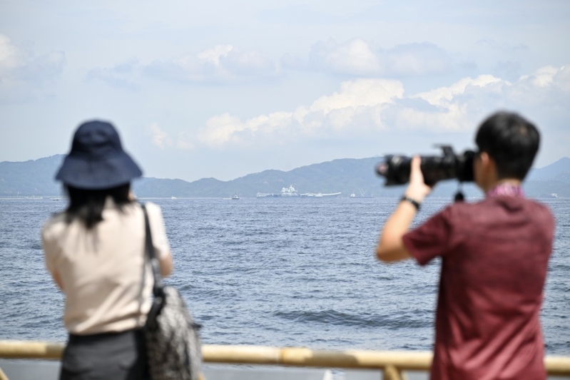 不少市民游客在坚尼地城海傍远眺山东舰。