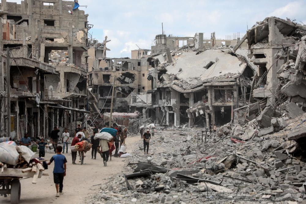 10月12日,在加沙地带南部汗尤尼斯,重返家园的巴勒斯坦人走过严重受损的建筑。新华社发(里泽克·阿卜杜勒贾瓦德摄)