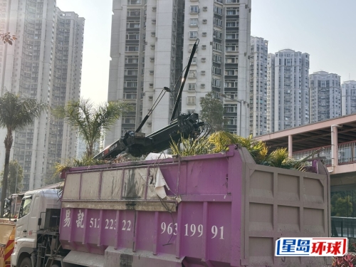 一辆盛满残断树枝的吊臂车，其吊臂在空中勾住了横跨马路两边的轻铁架空电缆。 梁国峰摄