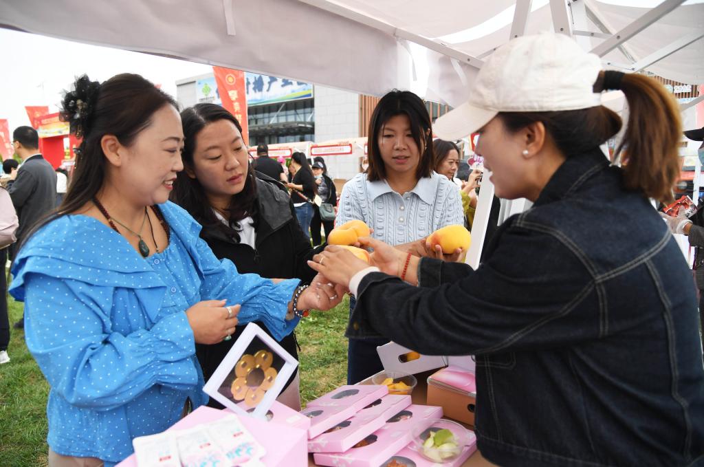  9月19日，北京市平谷区举办2025年中国农民丰收节暨第36届北京农民艺术节“乡村大舞台”平谷区专场展演。工作人员（右一）在活动现场向市民介绍农产品。新华社记者 任超 摄